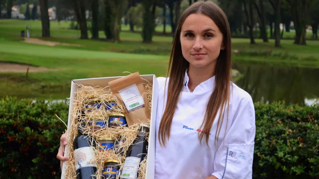 Coffret gourmand ouvert, produits calés dans la paille, présenté par une membre de l'équipe Panier de Région